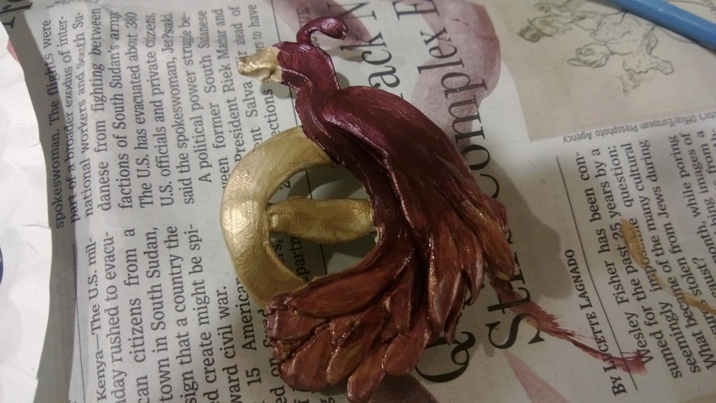 A clay phoenix pin painted red and gold.